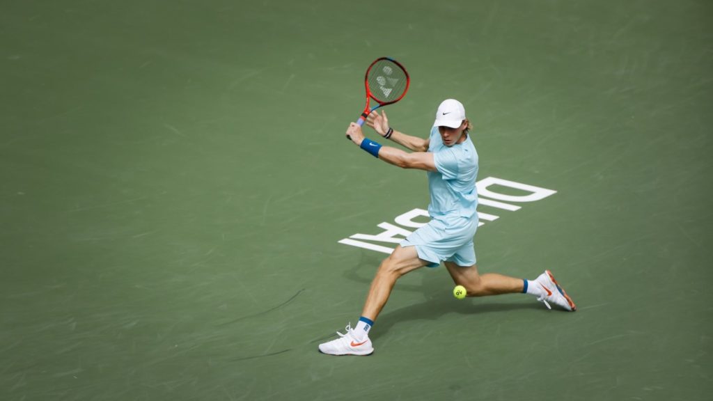 Denis Shapovalov hits a backhand slice with Dubai written on the ground behind him