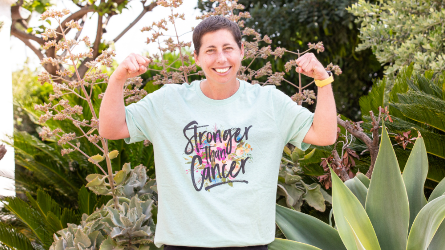 Carla Suarez Navarro smiles and flexes her arms, wearing a shirt that reads Stronger Than Cancer