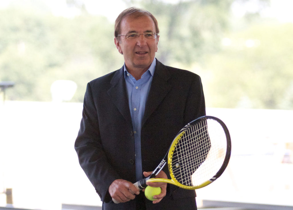 Louis Borfiga in a suit holding a tennis racket and a ball