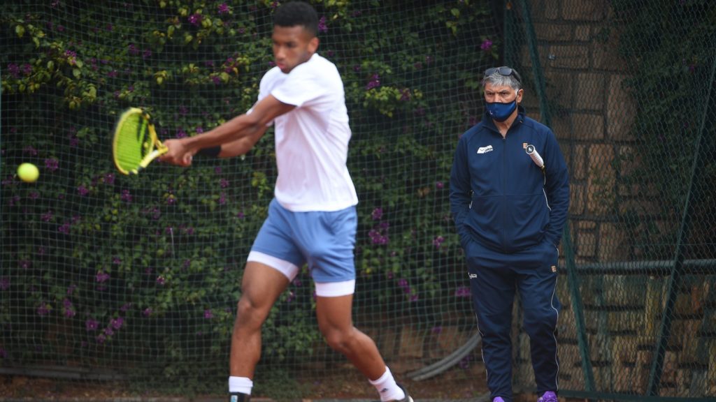 Felix Auger Aliassime hits a backhand on a clay court as Toni Nadal watches him