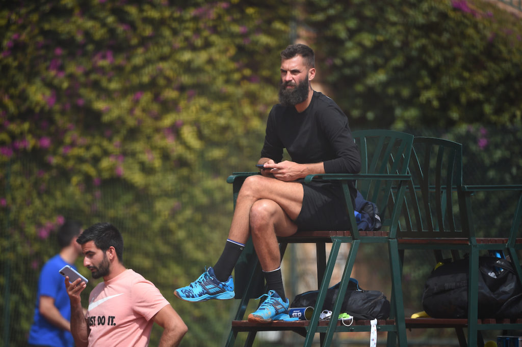 benoit paire sitting on the chair umpire's chair with crossed legs and a phone in his hands