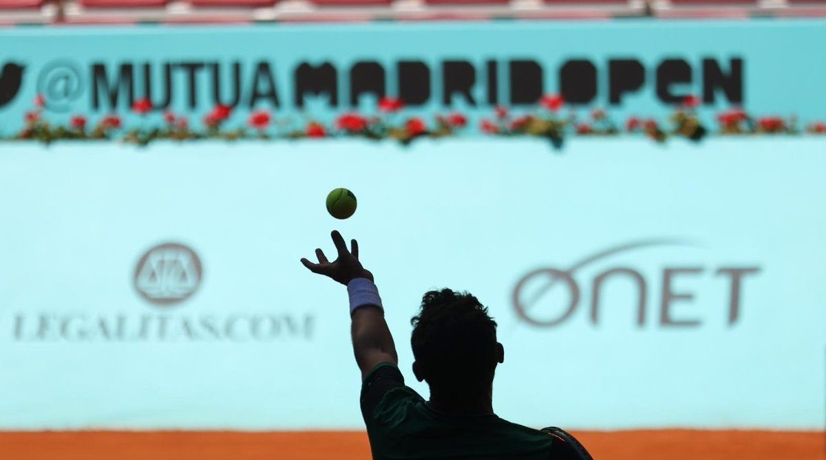 Player tosses ball up, mutua madrid open lettering in the background