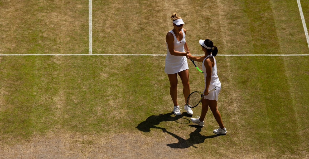 Gaby Dabrowski and Xu Yifan talk on a worn out grass court during a match