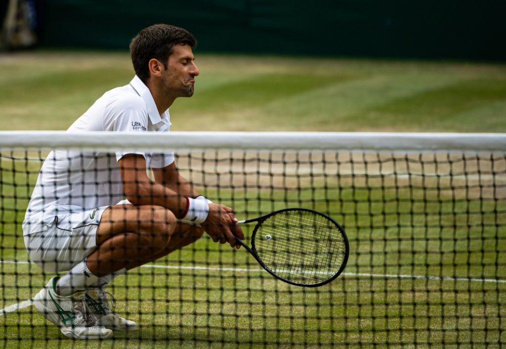 Novak Djokovic crouching on the Wimbledon Centre Court with an approval expression on his face
