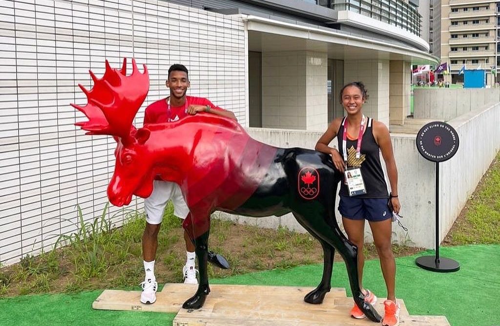 Félix and Leylah pose for a photo by a Moose statue painted with black and red, Team Canada's colours