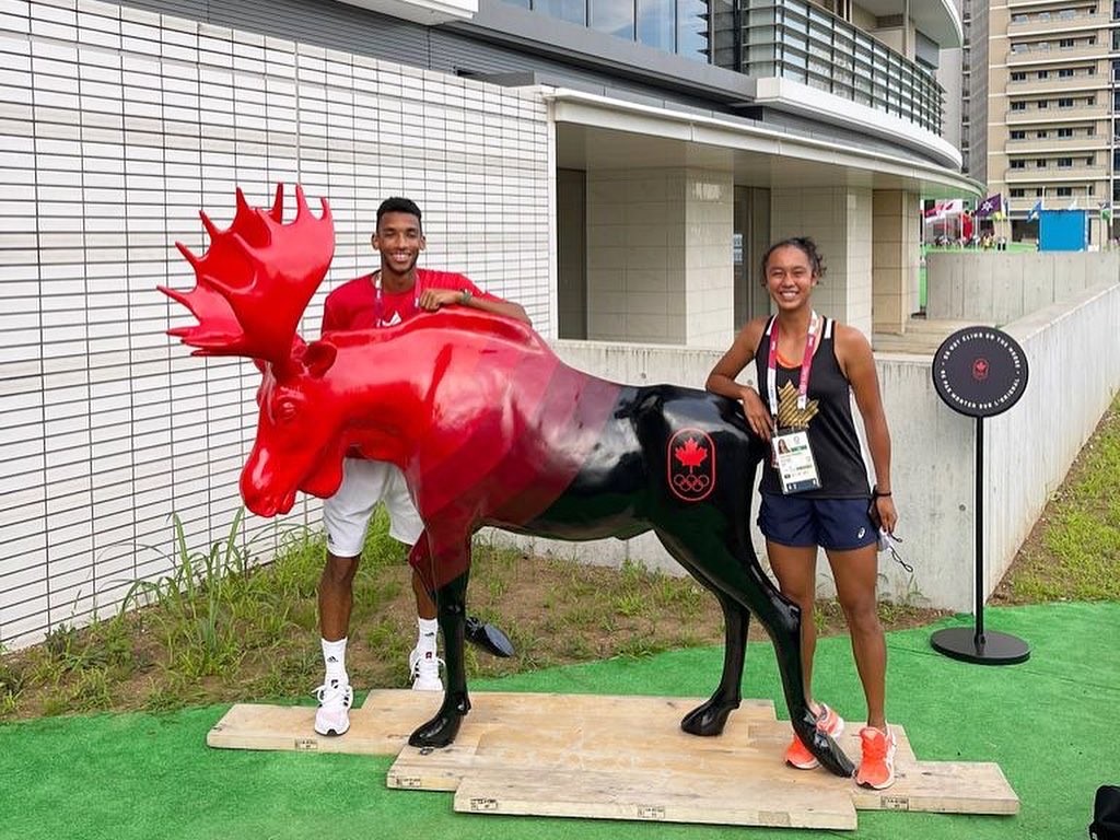Félix and Leylah pose for a photo by a Moose statue painted with black and red, Team Canada's colours