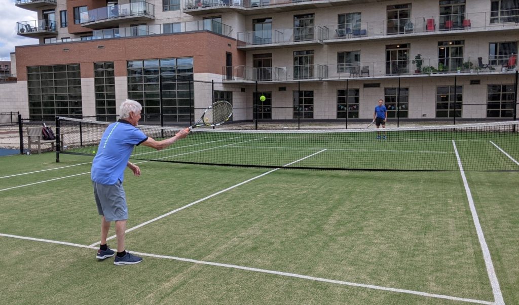 A senior man plays tennis on a grass court