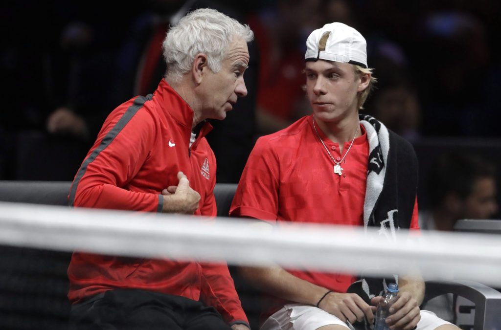 John McEnroe (left) leans in and talks to Denis Shapovalov