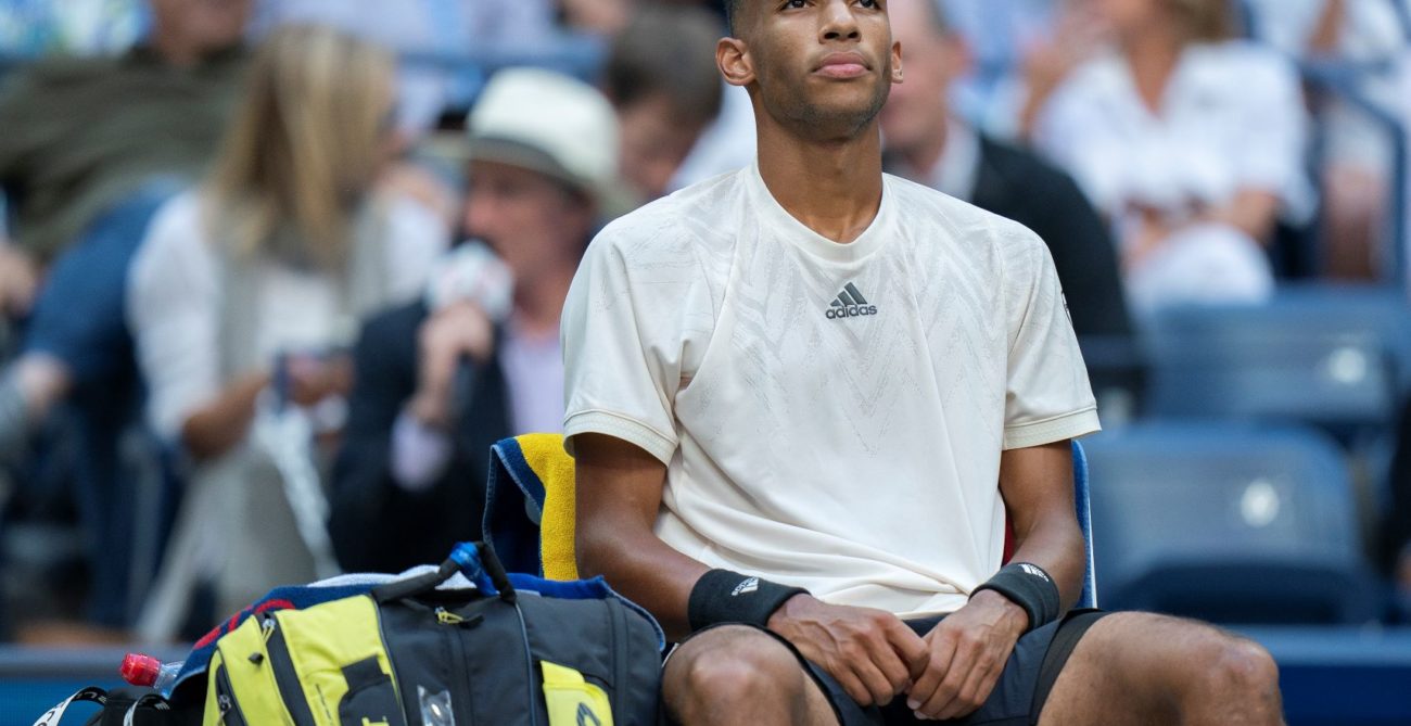 Felix Auger-Aliassime sits in his chair and stares off into the distance.