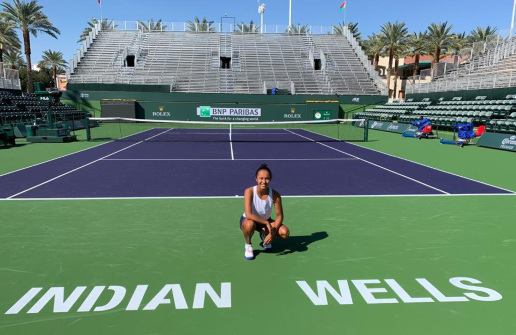 Leylal Fernandez kneels just above the Indian Wells sign on a court.