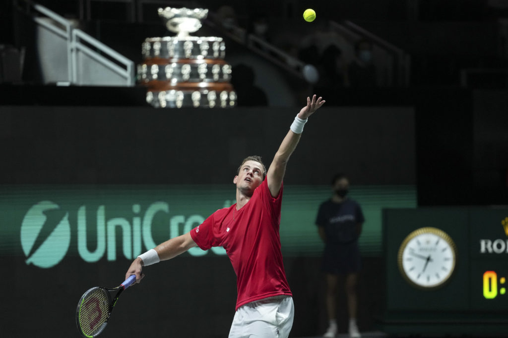 Vasek Pospisil serves with the Davis Cup trophy in the background.