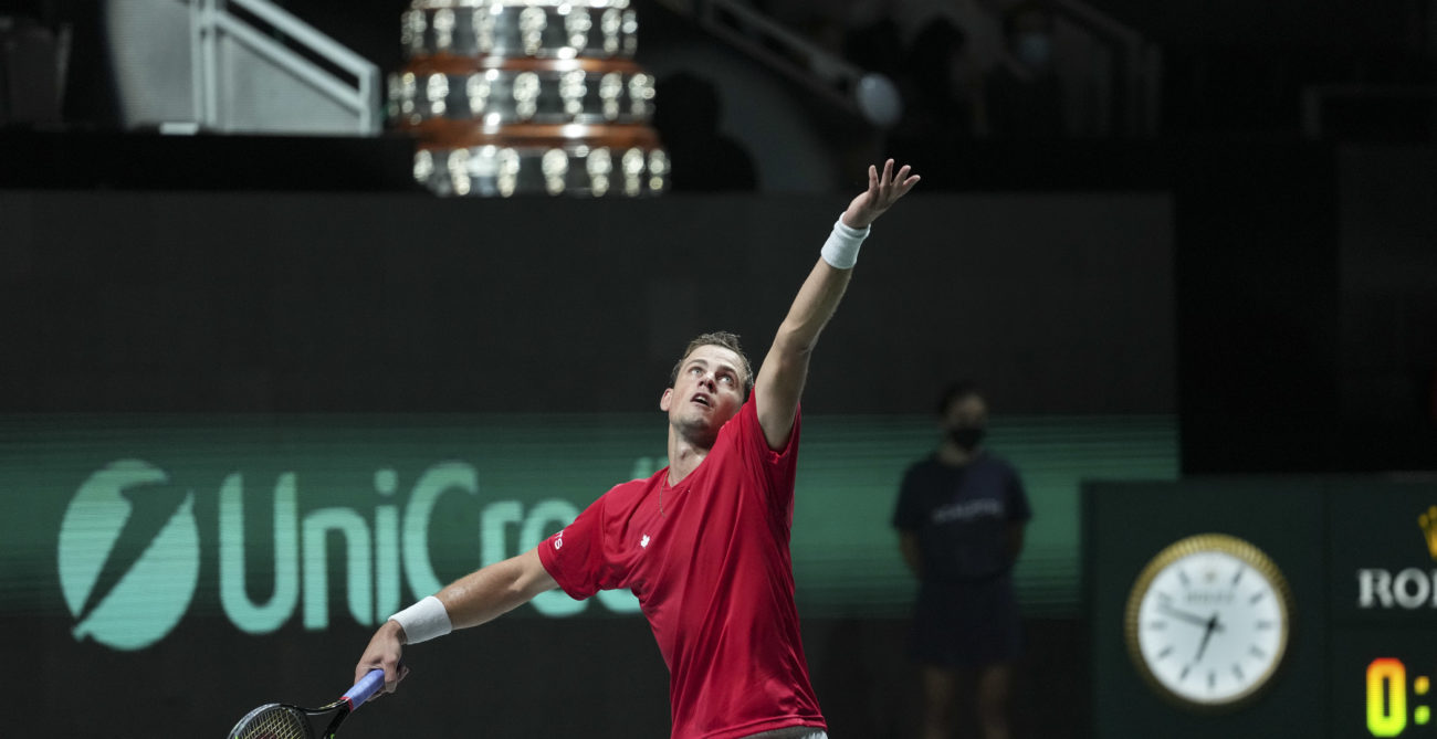 Vasek Pospisil serves with the Davis Cup trophy in the background.