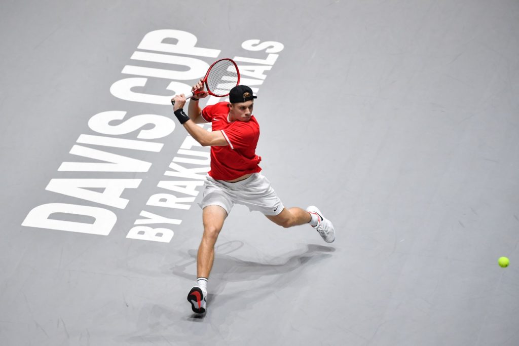 Denis Shapovalov runs to hit a backhand during a Davis Cup tie. Words Davis Cup by Rakuten written on the ground