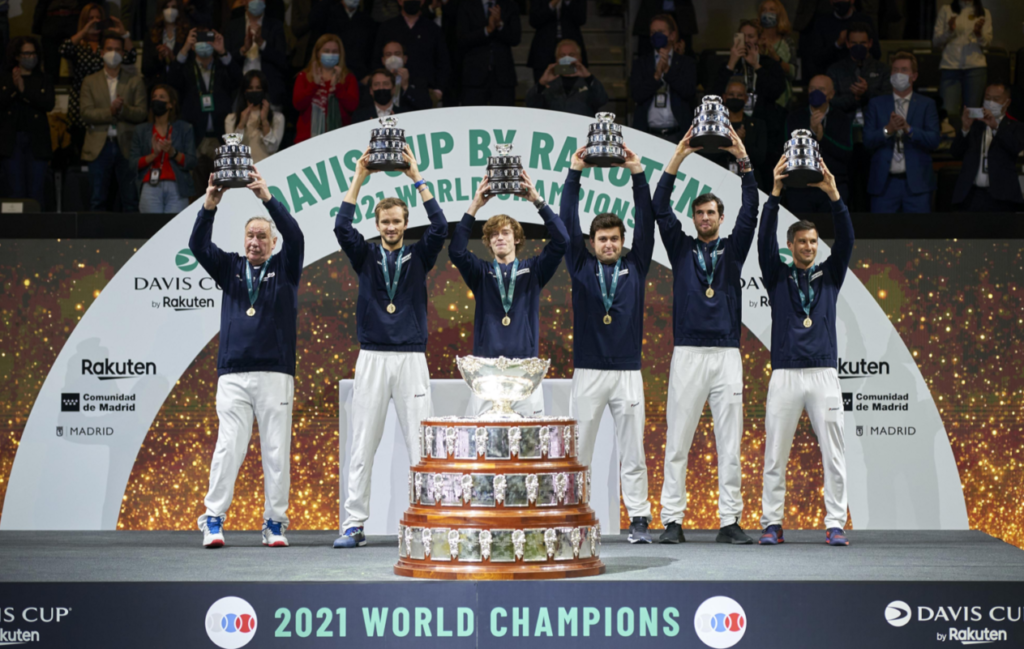The Russian Davis Cup team stands on a stage behind the trophy and lift their trophies.