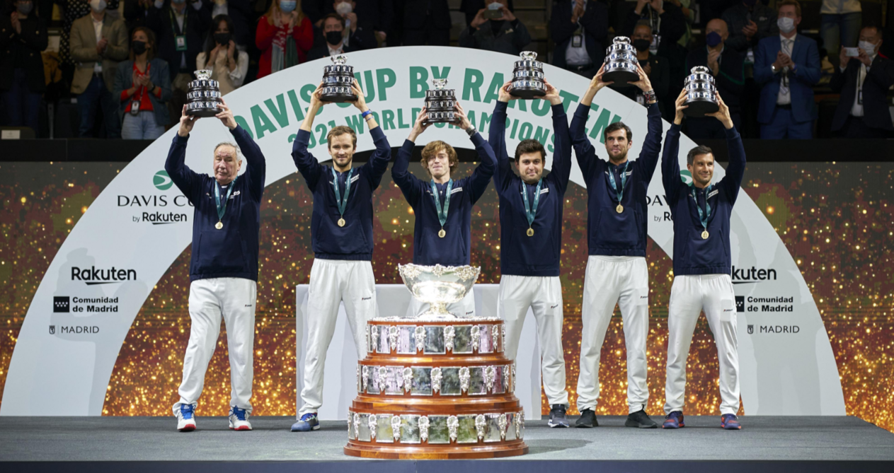 The Russian Davis Cup team stands on a stage behind the trophy and lift their trophies.