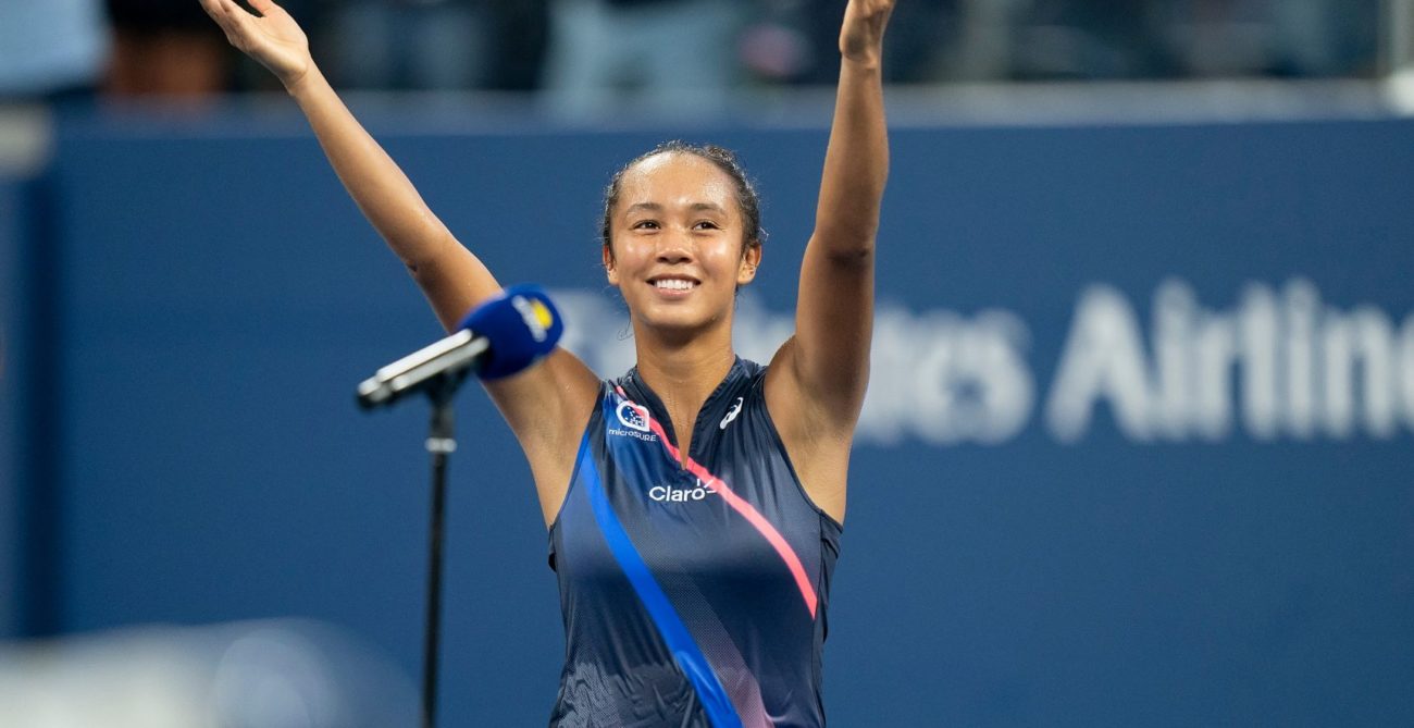 Leylah Fernandez standing in front of a mic on court and lifting her arms and smiling