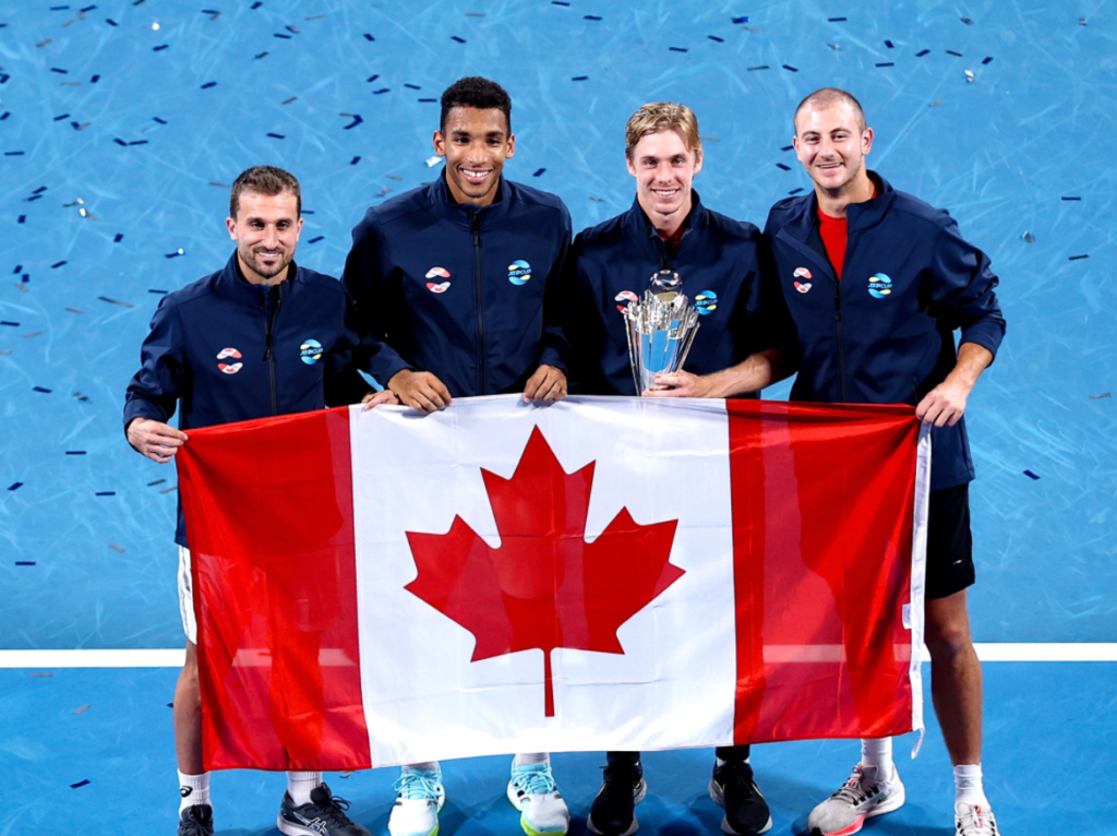 Steven Diez, Felix Auger-Aliassime, Denis Shapovalov and Brayden Schnur hold up the Canadian flag standing on the court while Shapovalov holds the ATP Cup trophy.