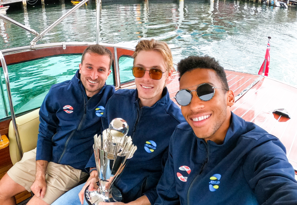 Steven Diez, Denis Shapovalov holding the ATP Cup trophy, and Felix Auger-Aliassime sit on a boat.