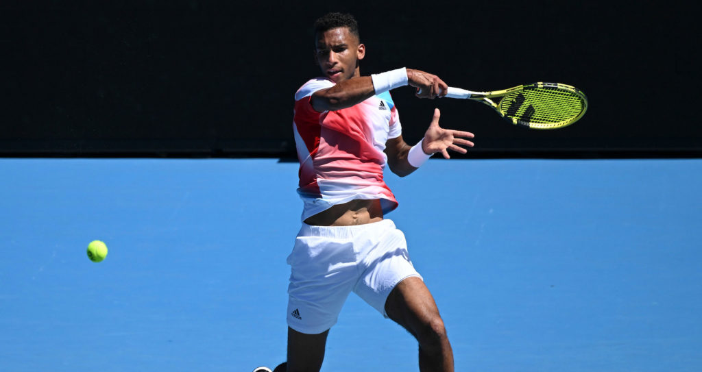 Auger-Aliassime leaps into the air as he follows through on a forehand.