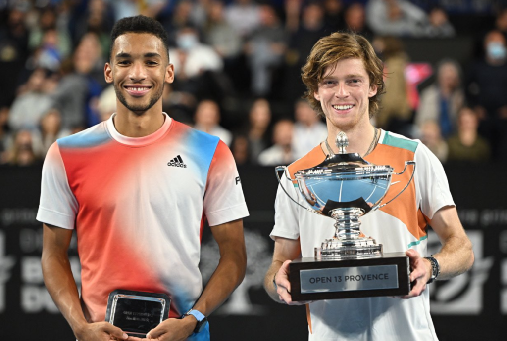 Felix Auger-Aliassime and Andrey Rublev hold their trophies and smile.