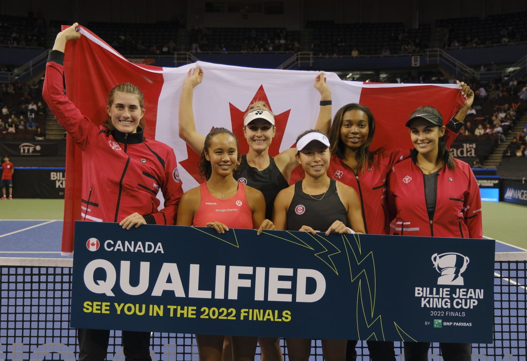 Team Canada stands behind the net holding a sign that reads "qualified" while holding the flag behind them.
