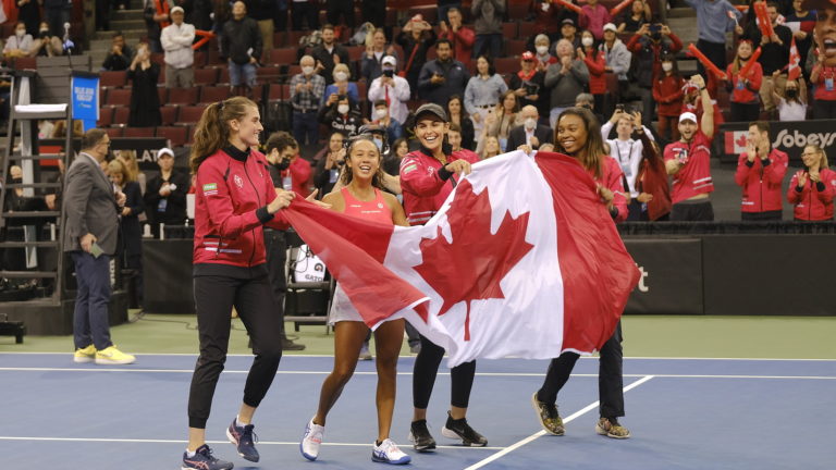 Rebecca Marino, Leylah Fernandez Heidi El-Tabak and Francoise Abanda hold the Canadian flag on court.