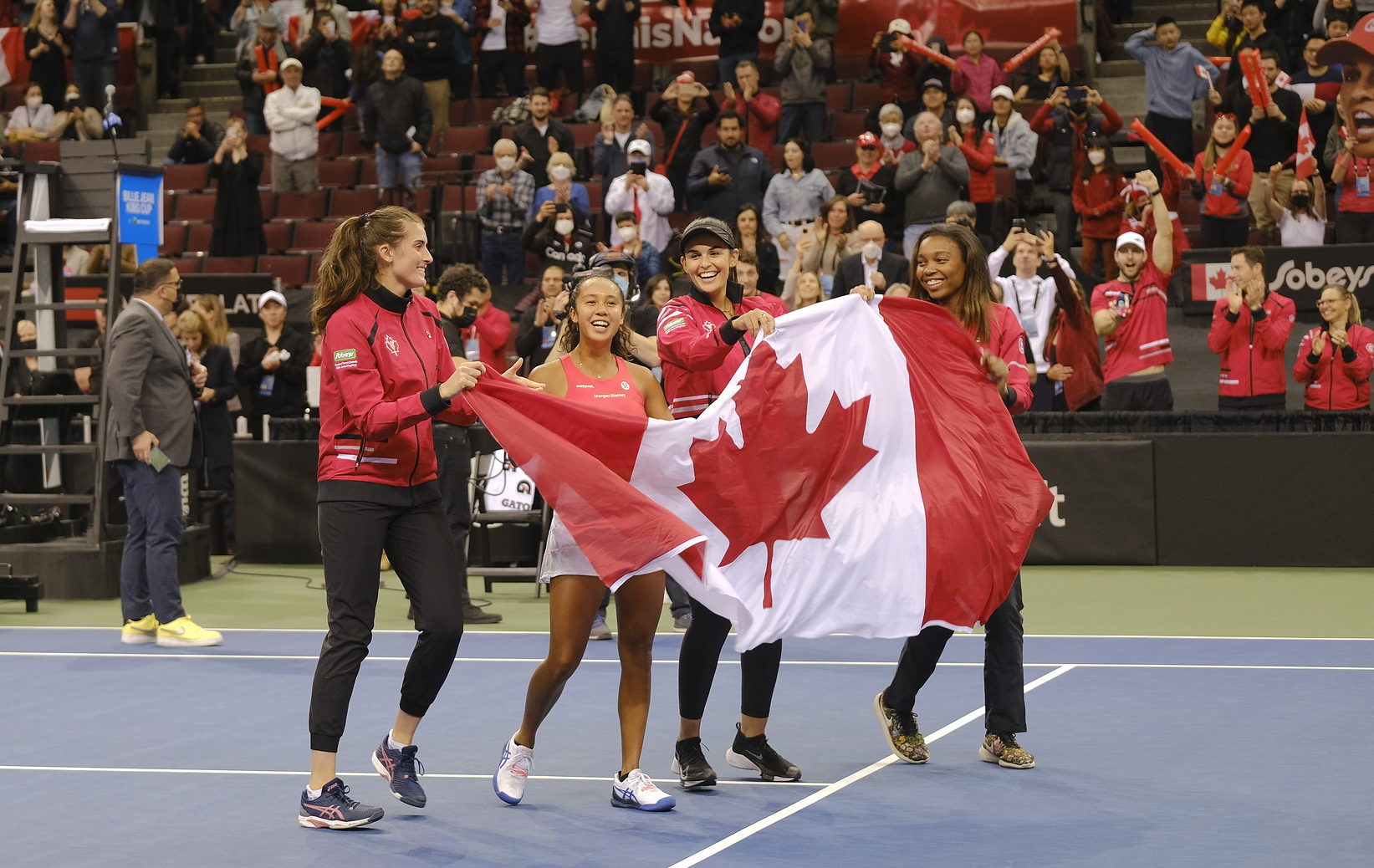 Rebecca Marino, Leylah Fernandez Heidi El-Tabak and Francoise Abanda hold the Canadian flag on court.