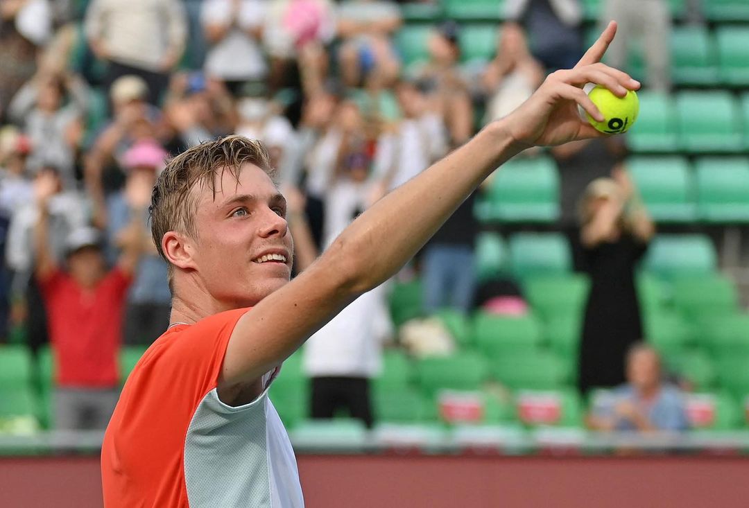 Shapovalov points finger to the sky while holding a ball and smiles
