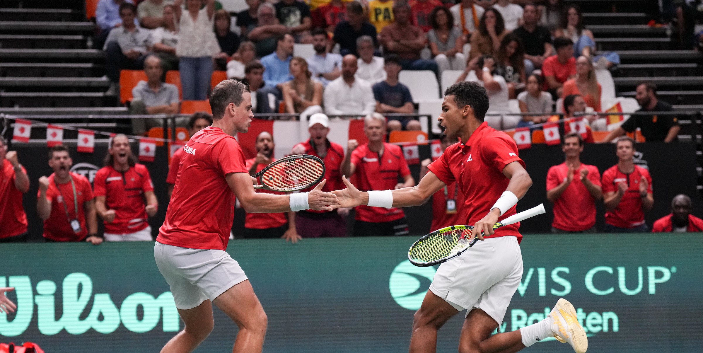 Vasek Pospisil (left) high fives Felix Auger-Aliassime in front of the Team Canada bench.