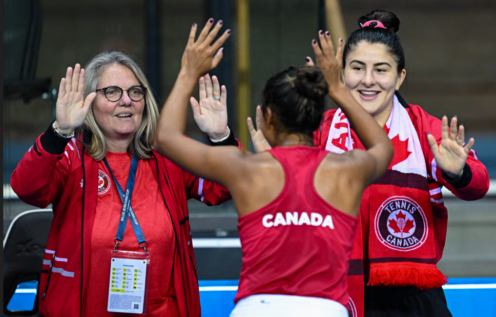 Leylah Fernandez (back to camera) high fives Bianca Andreescu and a team coach.