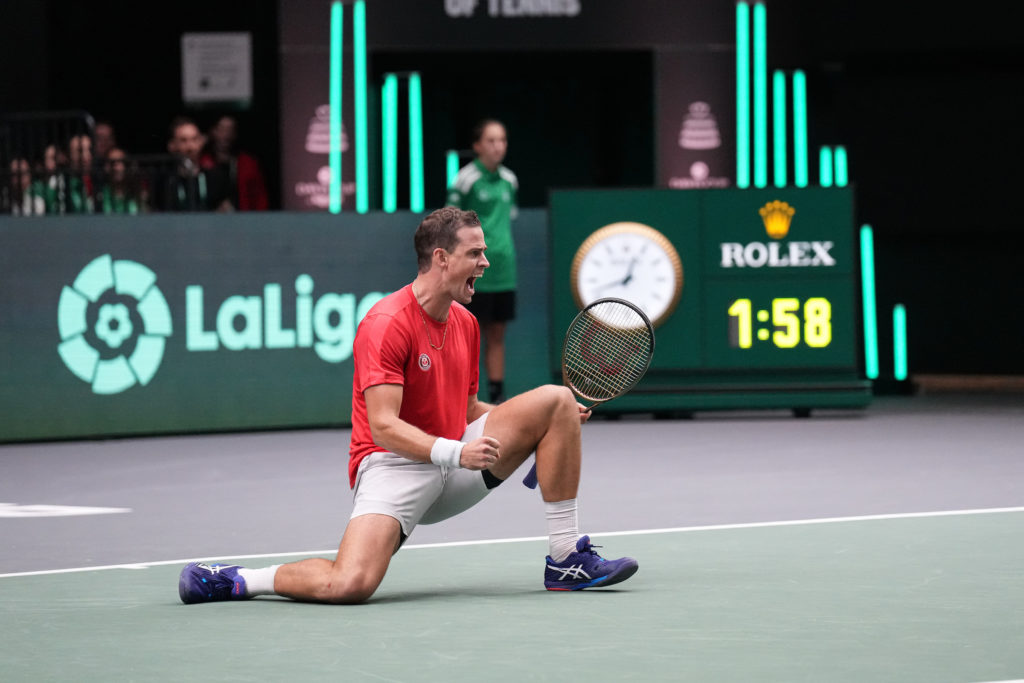 Vasek Pospisil kneels on the court, pumps his fist and shouts.