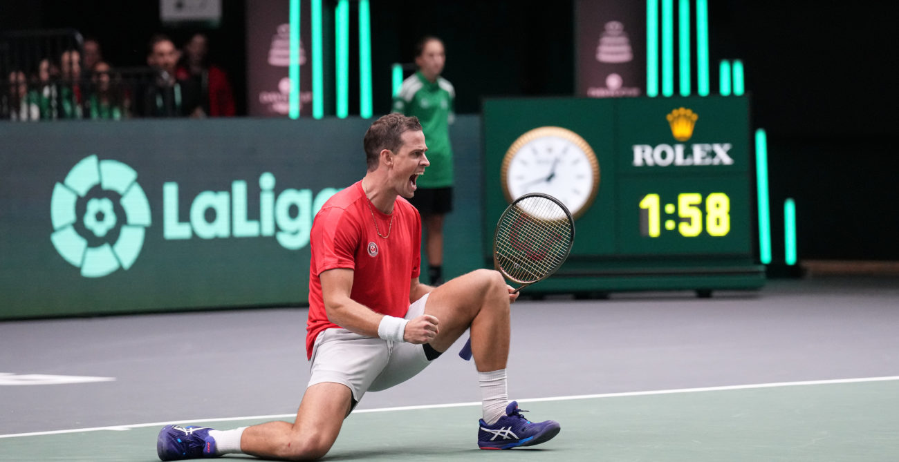 Vasek Pospisil kneels on the court, pumps his fist and shouts.