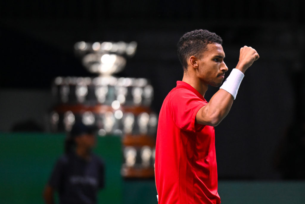 Felix Auger-Aliassime pumps his fist with the Davis Cup trophy in the background.
