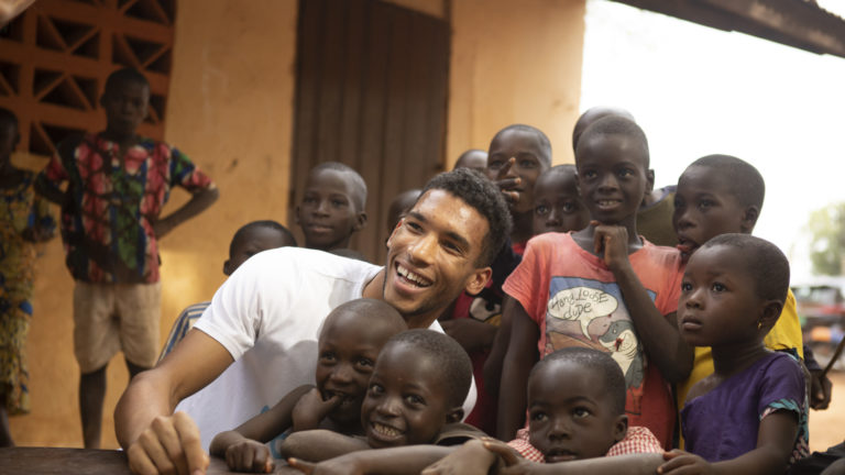 Felix Auger-Aliassime smiles while seated with a group of children in Togo.