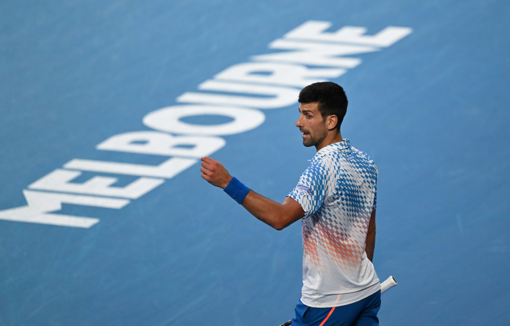 Novak Djokovic makes a gesture with his hand in front of the Melbourne sign on the court.