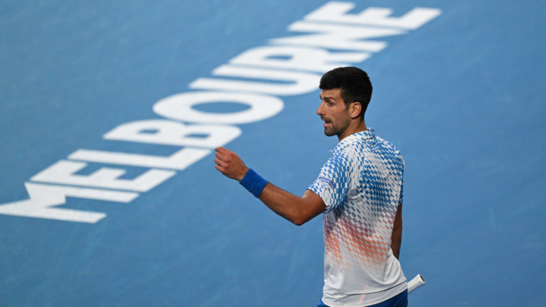 Novak Djokovic makes a gesture with his hand in front of the Melbourne sign on the court.