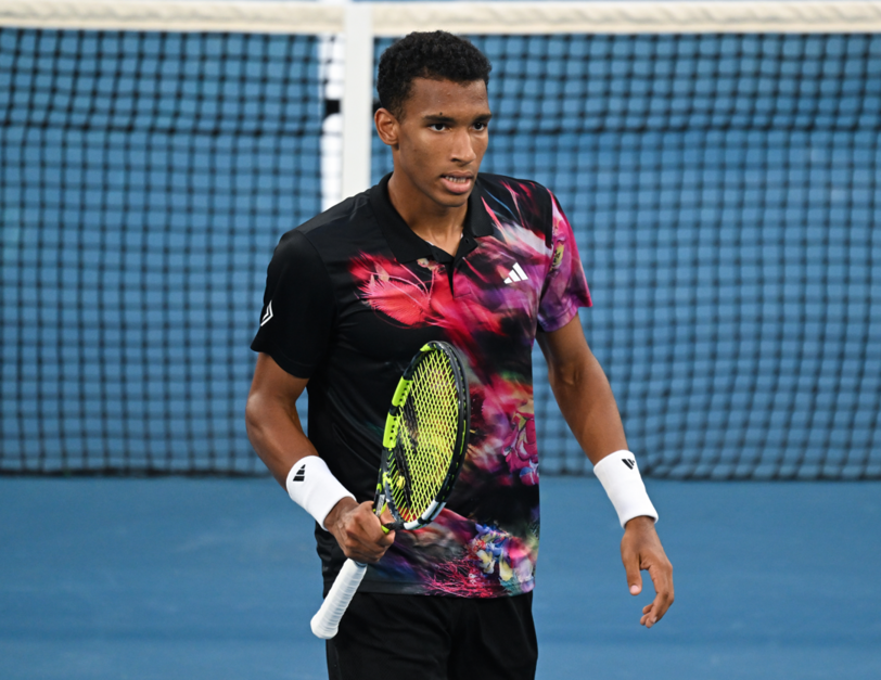 Felix Auger-Aliassime stands on the court by the net.