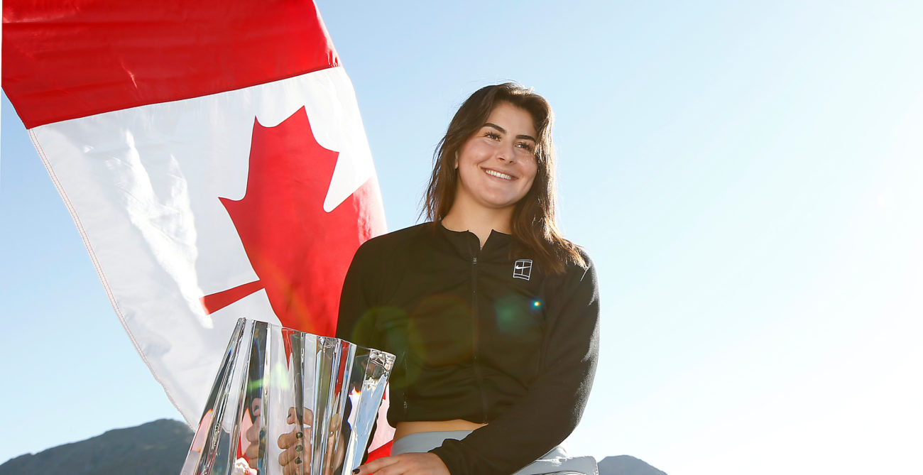 Bianca Andreescu sits with the Indian Wells trophy in front of the Canadian flag.