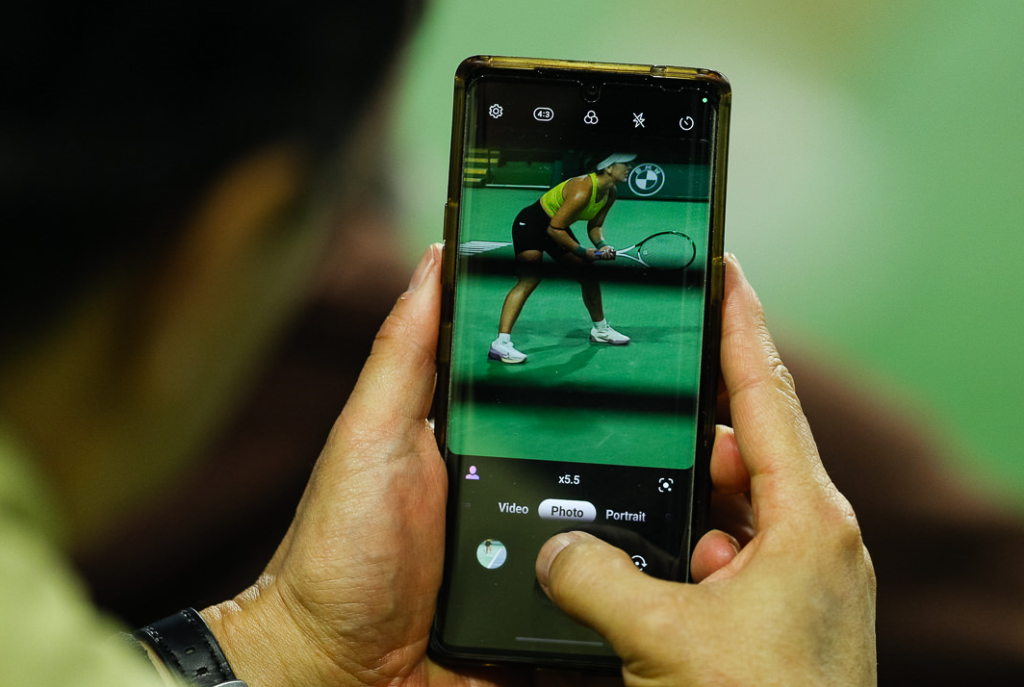 A fan holds a cameraphone and is taking a picture of Bianca Andreescu, visible on the phone screen.