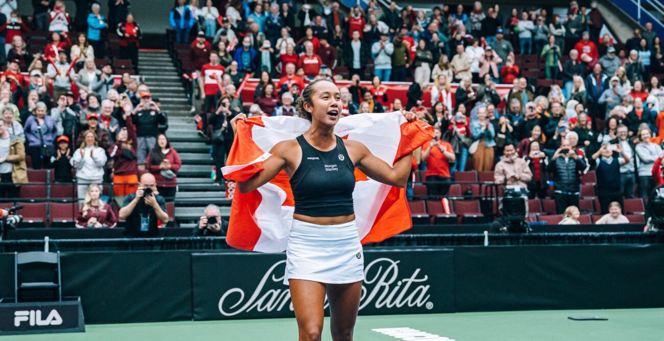 Leylah Fernandez walks on the court with the Canadian flag around her shoulders.