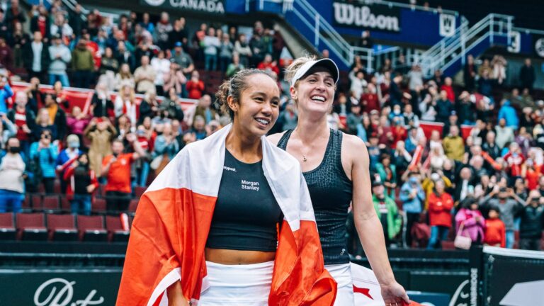 Leylah Fernandez (left) and Gabriela Dabrowski smile on court holding Canadian flags.