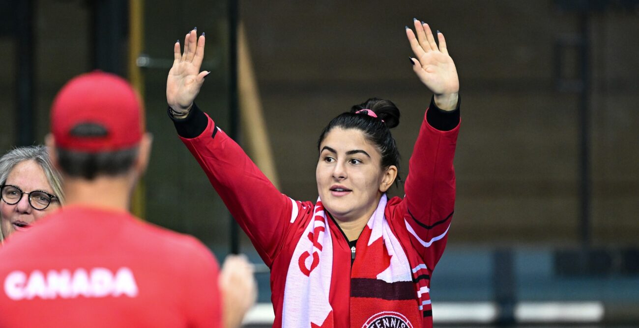 Bianca Andreescu stands on the Canadian bench and raises her hands over her head.