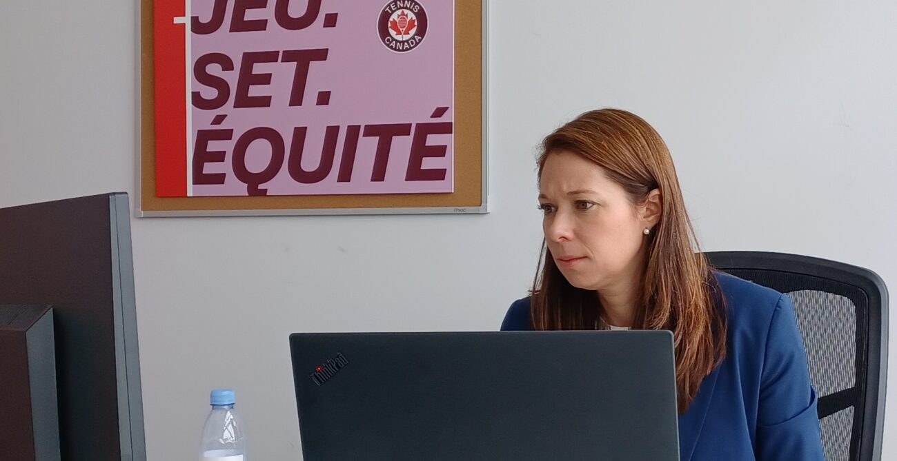 Val Tetreault sits at her desk in front of a "Game. Set. Equity" sign.