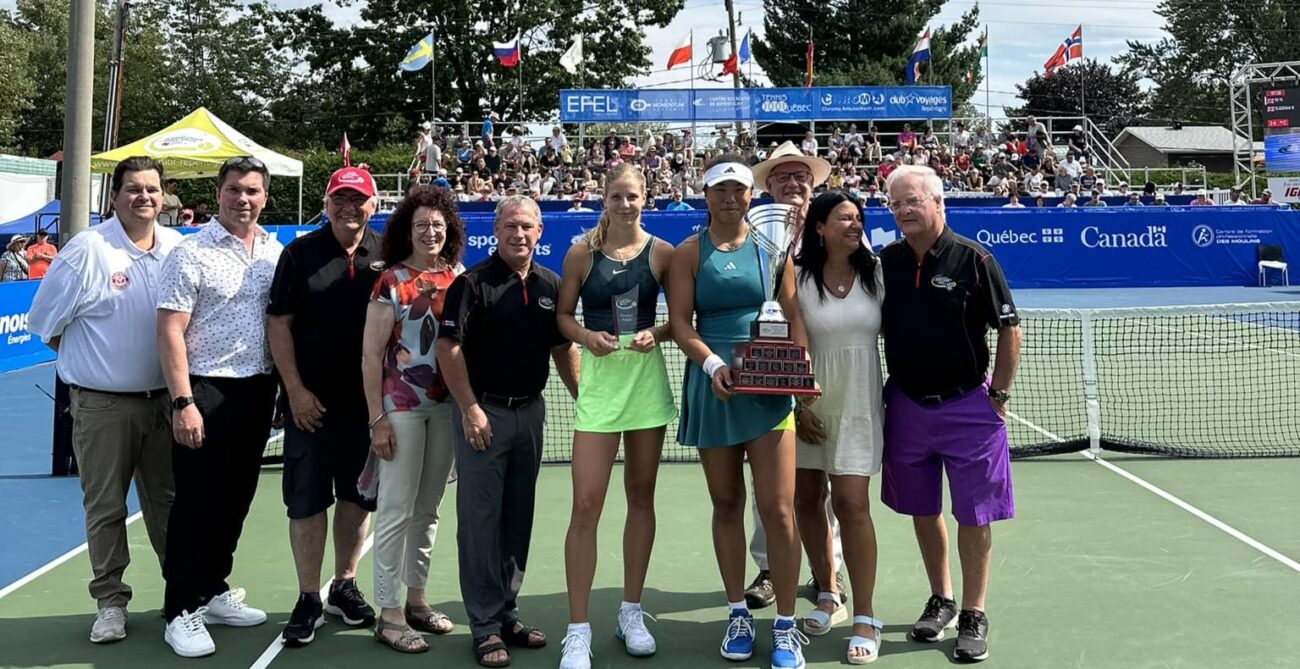 A row of people stand next to the two girls singles finalists with their trophies.