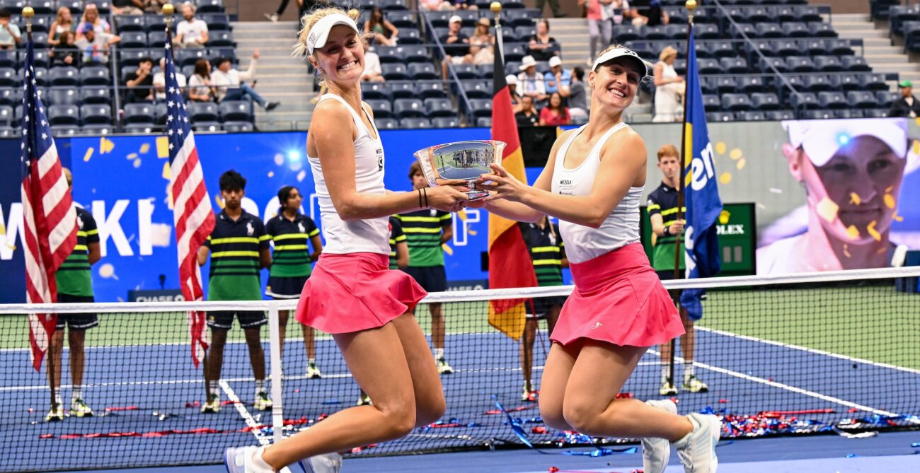 Gabriela Dabrowski (right) and Erin Routliffe jump in the air while holding the US Open doubles trophy between them.