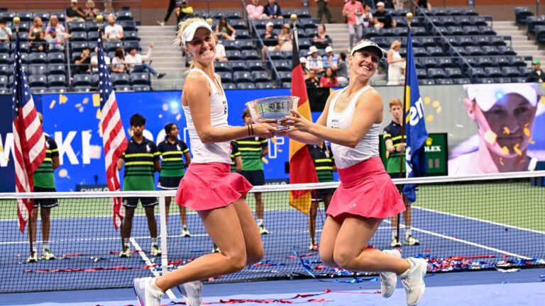 Gabriela Dabrowski (right) and Erin Routliffe jump in the air while holding the US Open doubles trophy between them.
