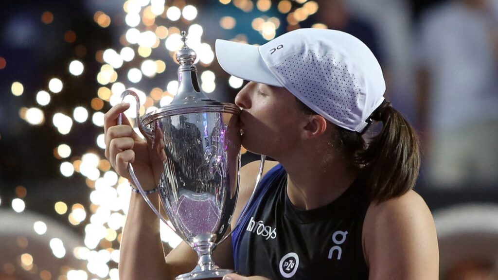 Iga Swiatek kisses the WTA Finals trophy.