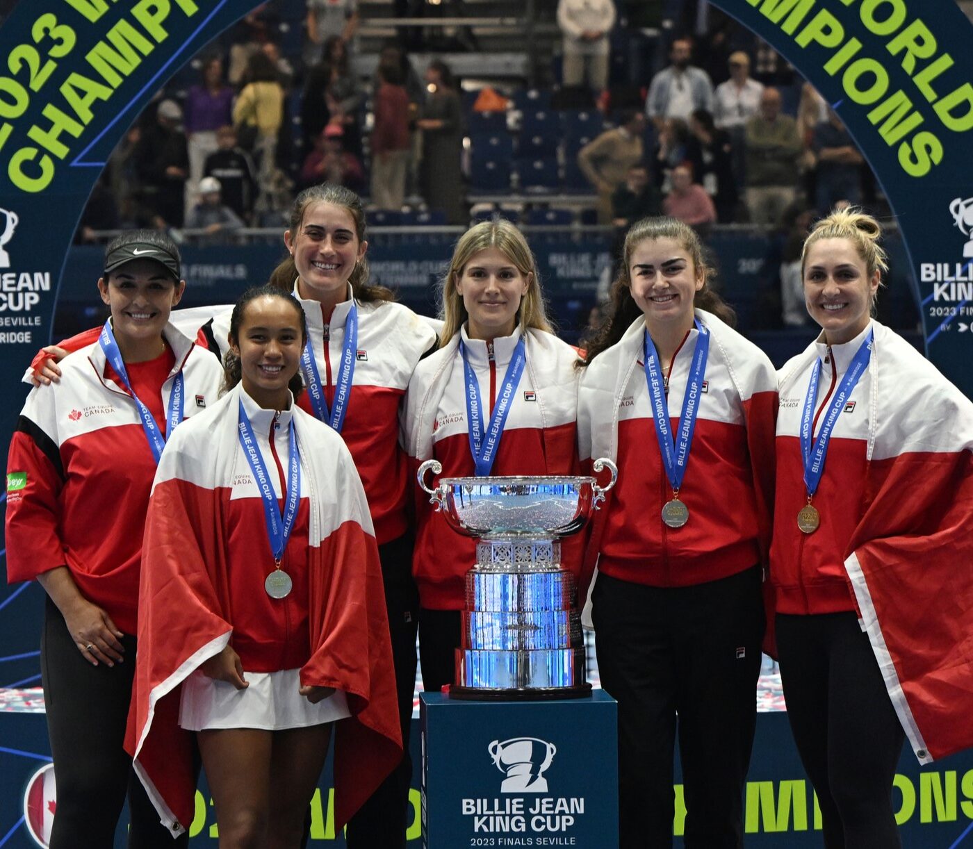 From left to right, Heidi El Tabakh, Leylah Fernandez, Rebecca Marino, Eugenie Bouchard, Marina Stakusic, and Gabriela Dabrowski wear their medals and stand behind the Billie Jean King Cup trophy.