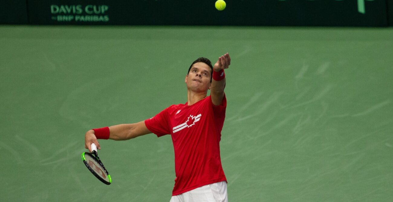 Milos Raonic tosses a ball up to serve while playing for Team Canada at the Davis Cup.